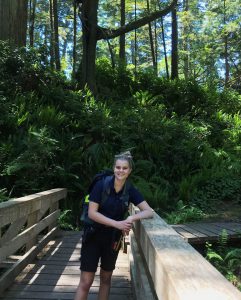 Student ranger leaning against a wooden bridge in front of a forest at Botanical Beach Provincial Park