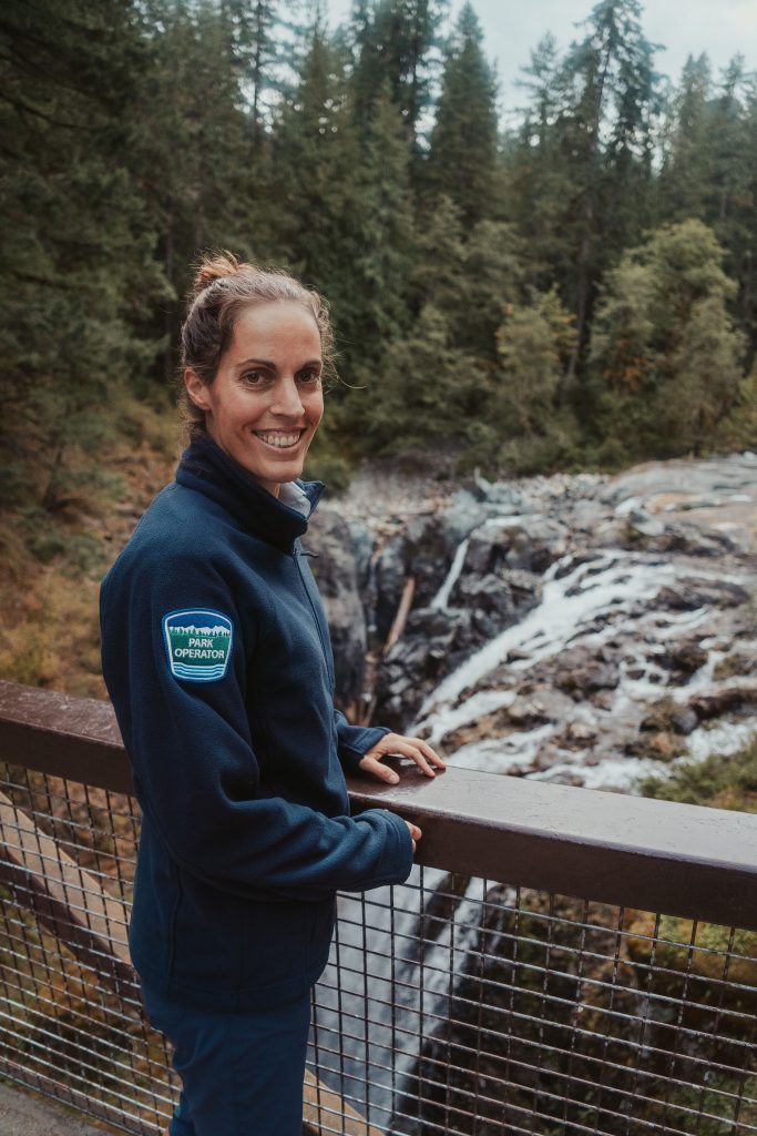 A person with a park operator uniform on standing at a railing beside a waterfall.