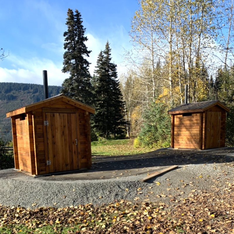 Photo of two new rustic wooden outhouses. 