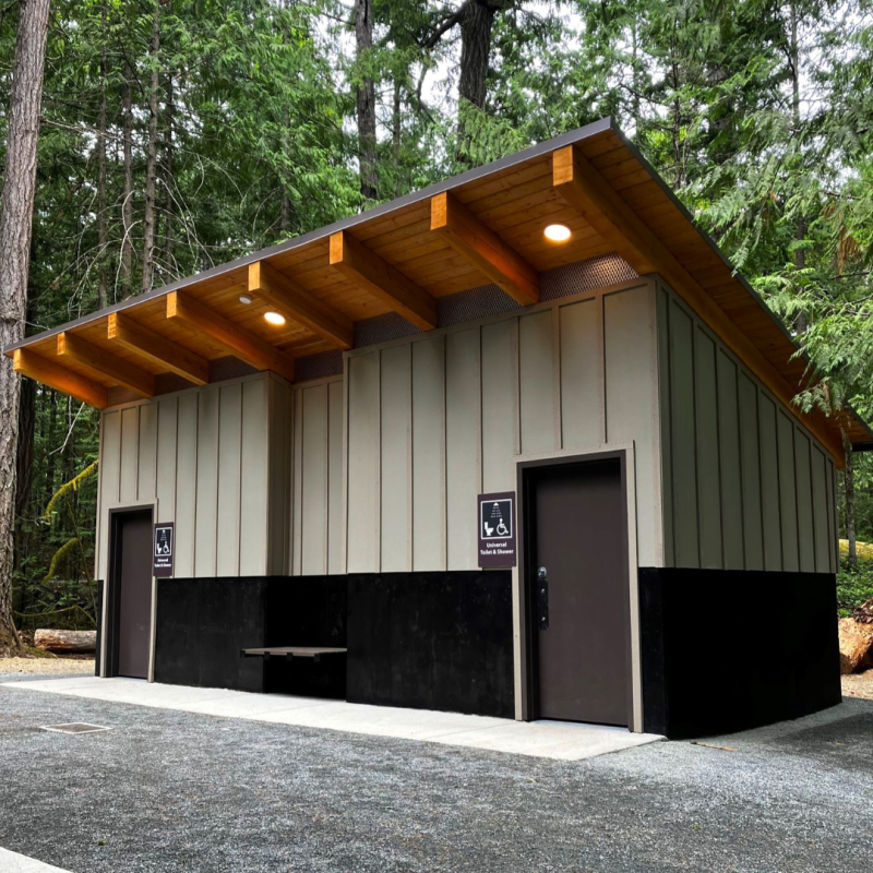 Photo of a modern outdoor washroom and shower facility with a slanted wooden roof and two doors. 